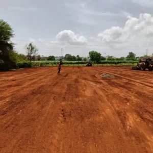 Sports ground under construction with red soil leveling for natural grass installation.